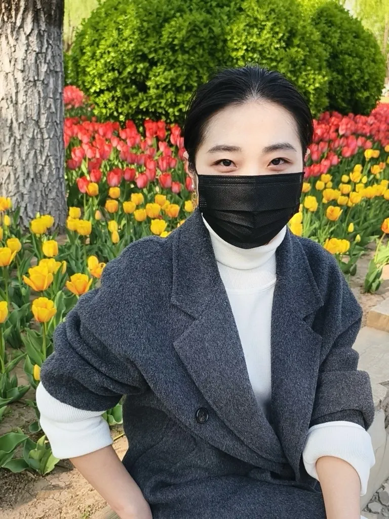 坐在花坛前的半身照，灰色大衣挽起袖口，身后是成片的黄色与红色郁金香